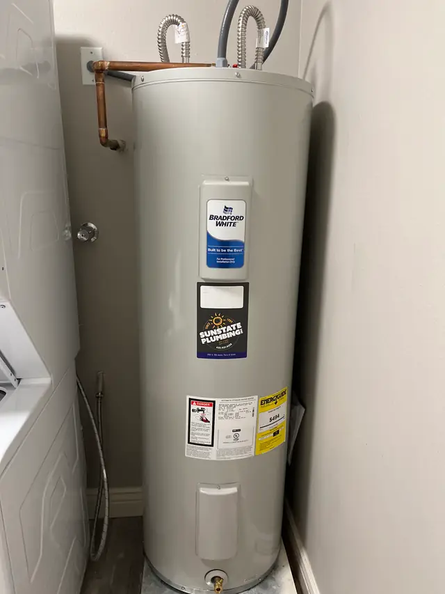 Electric tank water heater installed by Sunstate Plumbing in a laundry nook, Sunstate sticker on the tank